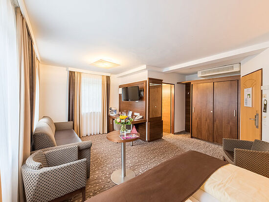 A room with a bed, a long couch, a TV and a large bathroom