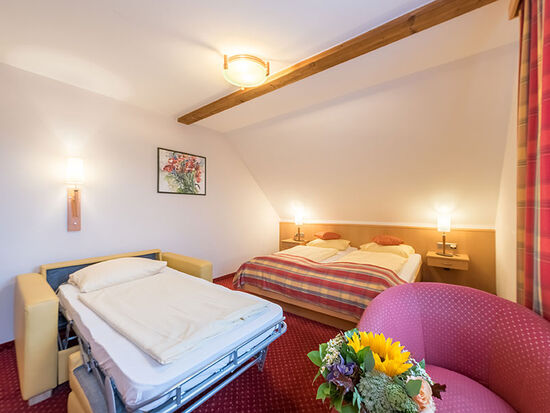 Das Doppelbett mit Fernseher und einem kleinen Tisch im selben Raum und eine ausgezogene Klappcouch ziert den Raum