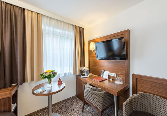 Two comfortable armchairs look under the TV, in the middle of the room there is a small table on it with fresh flowers.