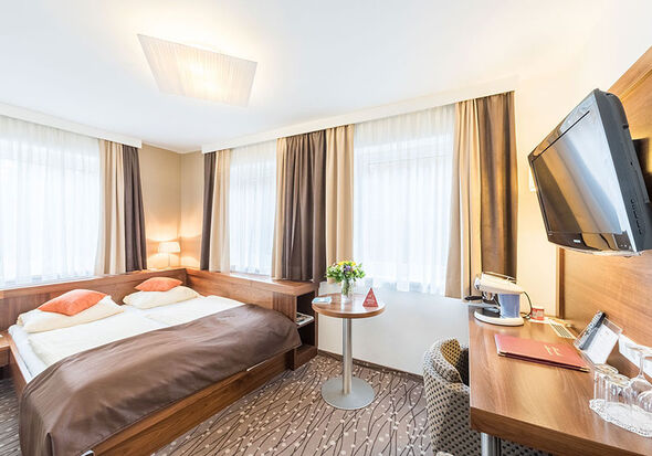 Ein Doppelbett und ein kleiner Tisch stehen vor dem großen Fernseher und den Tisch befindet sich eine Kaffeemaschine.