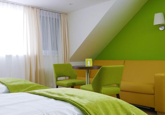 Das Hotelzimmer hat grüne Sessel und eine Gelbe Couch um es sich drauf bequem zu machen.
