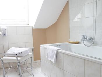 Eine große Badewanne ziert das Badezimmer und ein kleiner weißer Sessel steht daneben.