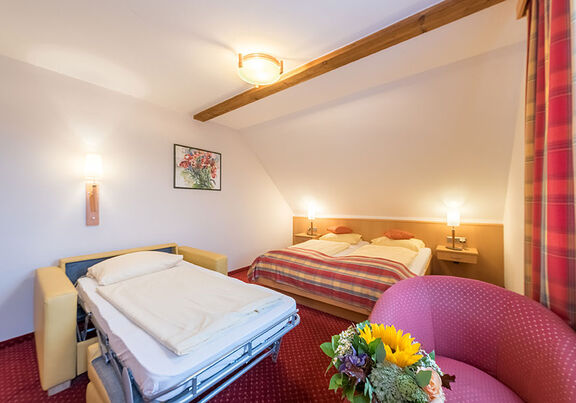 Das Doppelbett mit Fernseher und einem kleinen Tisch im selben Raum und eine ausgezogene Klappcouch ziert den Raum