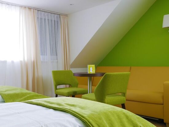 Das Hotelzimmer hat grüne Sessel und eine Gelbe Couch um es sich drauf bequem zu machen.