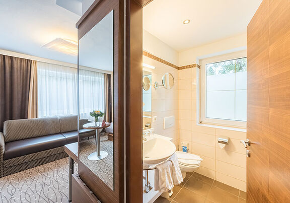 A room, a long couch, a TV and a large bathroom