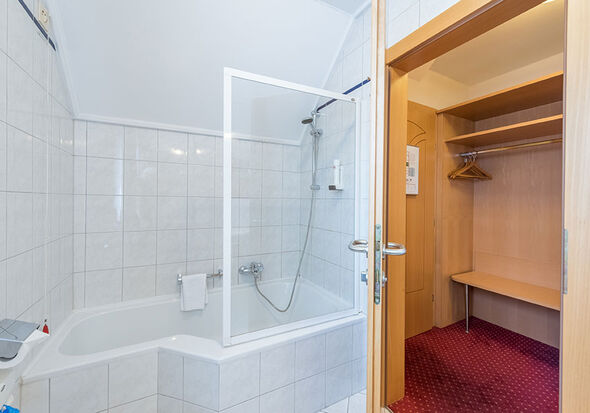 Das modern gehaltene Bad mit Badewanne und Dusche, rechts im Bild der geräumige Zimmerflur