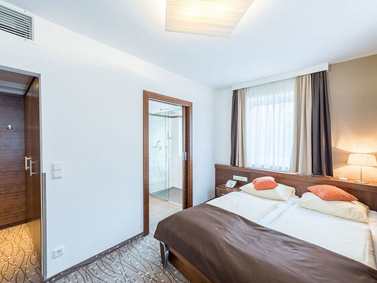 Ein Doppelbett und zwei Türen, eine Führt in das Badezimmer, die andere in den kleinen Flur.