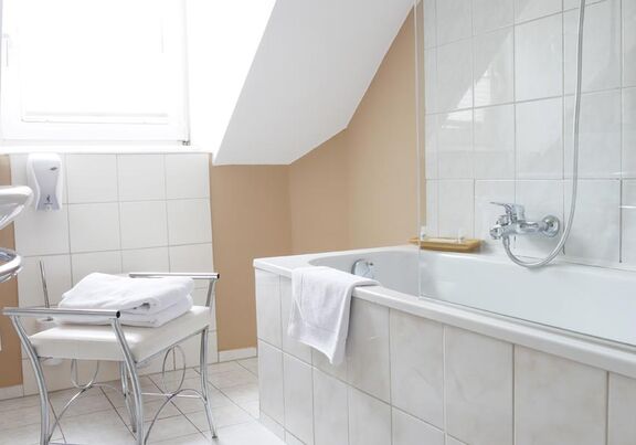 Eine große Badewanne ziert das Badezimmer und ein kleiner weißer Sessel steht daneben.