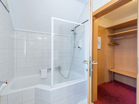 Das modern gehaltene Bad mit Badewanne und Dusche, rechts im Bild der geräumige Zimmerflur